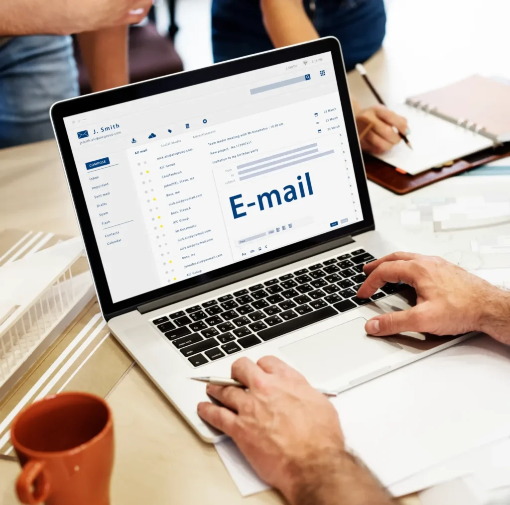 Laptop showing a business email inbox on a desk in a busy office