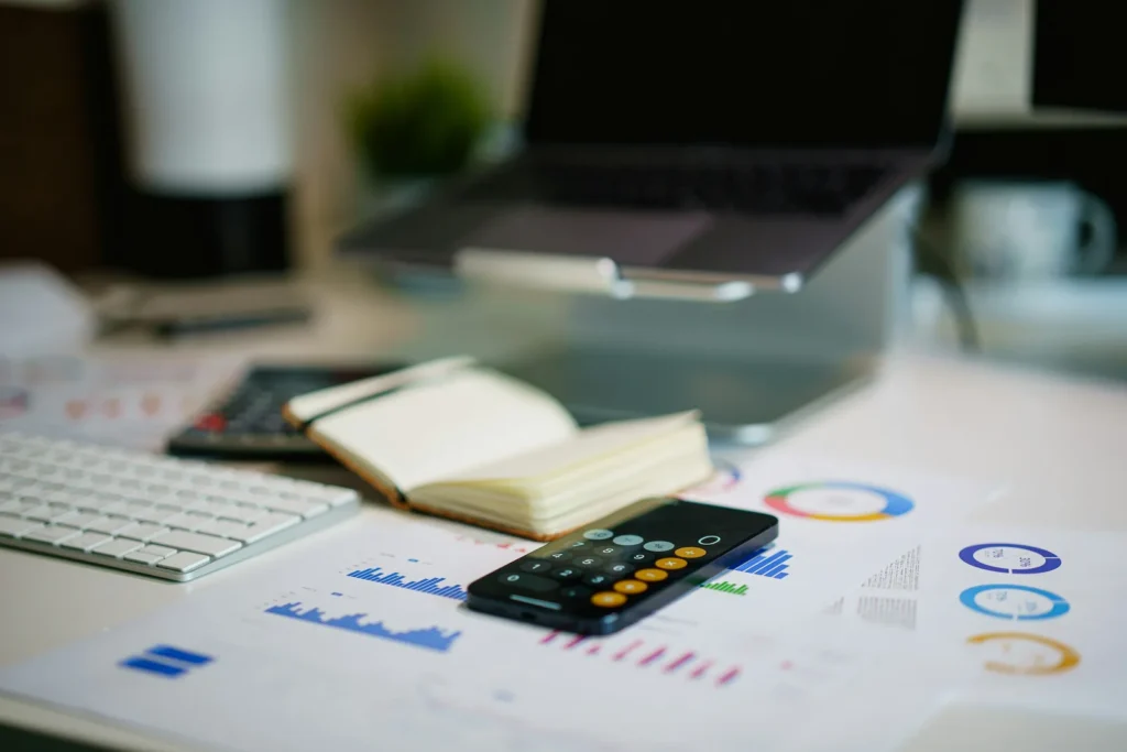 Calculator, printed charts and a laptop on a desk while budgeting for a website